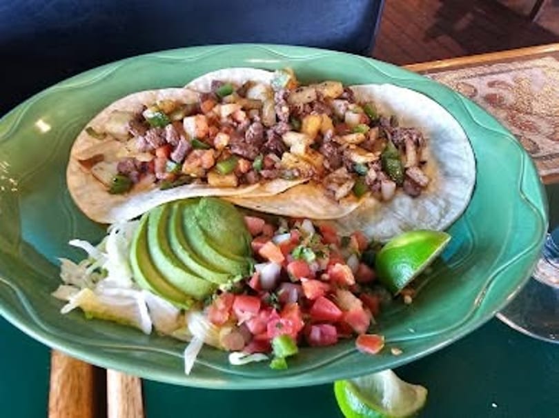 Two street tacos with meat, potatoes, and peppers, served with avocado, pico de gallo, and lime.