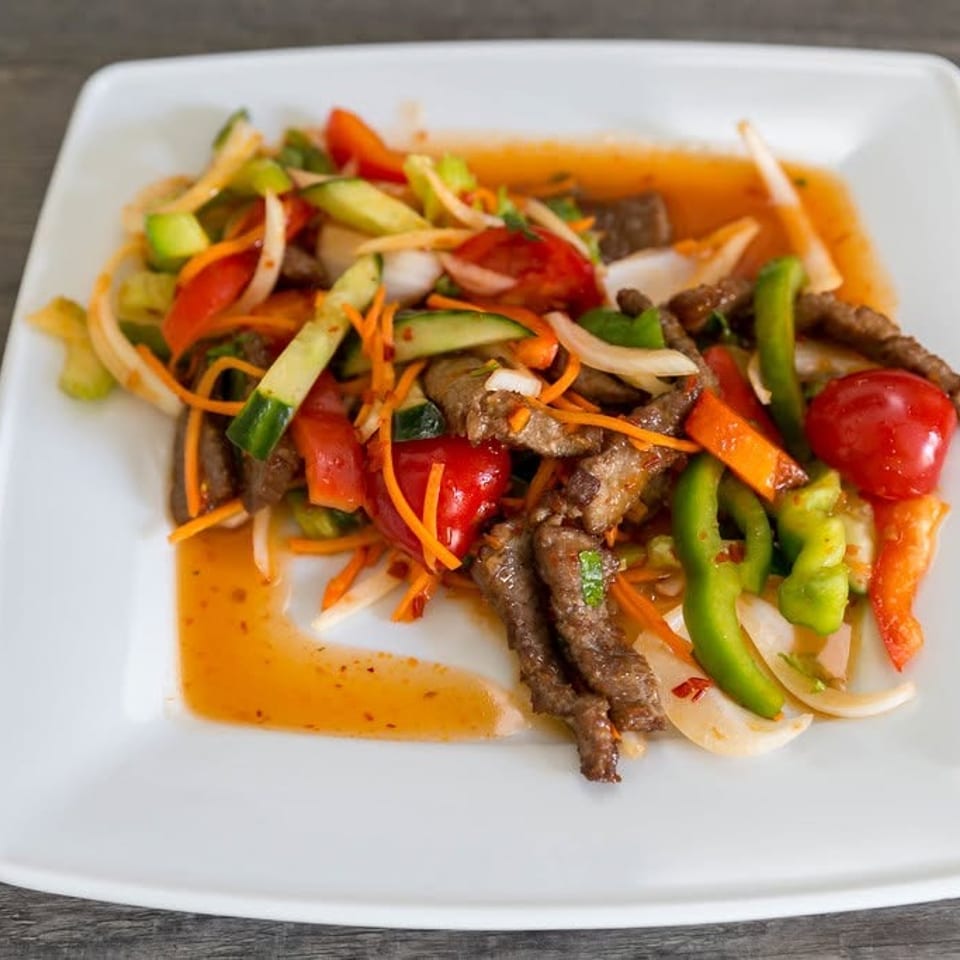 Spicy beef salad with sliced vegetables like bell peppers, onions, and carrots on a white plate.